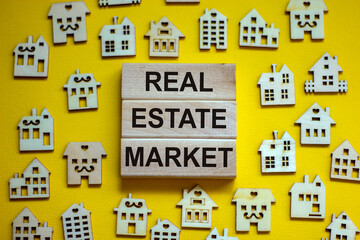 Wooden blocks form the words 'real estate market', miniature wooden houses. Beautiful yellow background, copy space. Business concept.