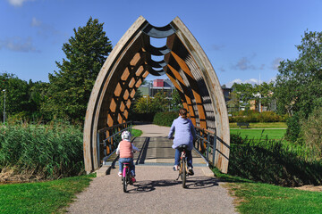 The mother and her daughter on the bicycles on the modern wooden pedestrian bridge in Helsinki,...