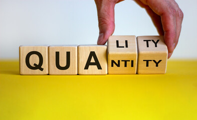 Quality over quantity. Hand turns cubes and changes the word 'quantity' to 'quality'. Beautiful yellow table, white background, copy space. Business concept.