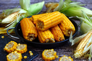 Close-up of ripe boiled corn and cobs on a wooden background.