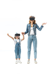 Fototapeta premium mother and daughter in denim outfits and virtual reality headsets holding hands isolated on white