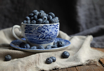 Original vintage style food photograph of a blue teacup filled with fresh blueberries on a dark...