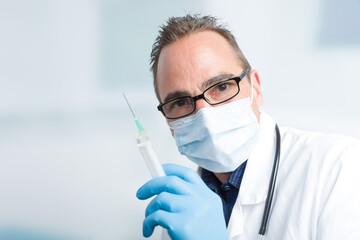 male doctor with medical face mask and medical gloves holds a syringe 