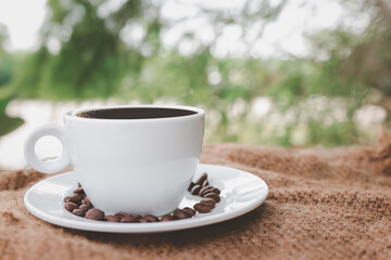 hot white coffee cup with coasters and coffee beans placed on brown burlap cloth on natural background.
