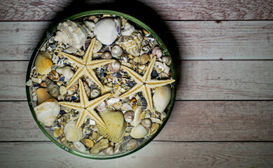 Glass bowl with starfish, shells and sand, on wooden background. Concept- holiday, souvenirs