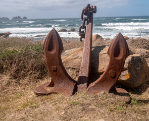 Fototapeta premium ENORMOUS ANCHOR OF ANCIENT BOAT ON THE GROUND WITH THE SEA BEHIND