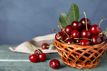 Sweet juicy cherries with leaves on wooden table against blue background, closeup. Space for text