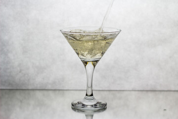In a Martini glass, standing on a white background, the drink is poured from above