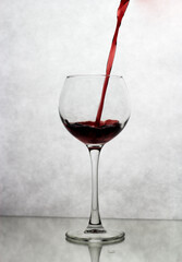 In a wine glass, standing on a white background, wine is poured from above
