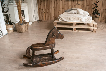 Fototapeta na wymiar Bedroom in the interior of wood with a wooden horse. There's a children's horse in the foreground. In the background is a bed and a fireplace. High quality photo.