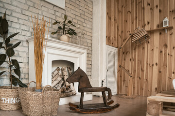Wooden rocking horse stands in a room by the fireplace. Nearby wicker baskets with plants. High quality photo.