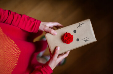 Christmas background with gift boxes, balls of rope, paper rolls and decorations on red. Preparing gifts for Christmas. Children's hands holding a gift box, top view.