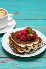 portion of Classic tiramisu dessert with raspberries and cup of espresso coffee on blue wooden background