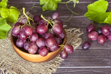 bunches of grapes in a wooden bowl, standing on sacking, close-up. pink grapes and vines. background with grapes.