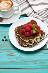 portion of Classic tiramisu dessert with raspberries and cup of espresso coffee on blue wooden background