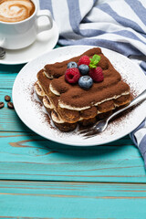 portion of Classic tiramisu dessert with raspberries and blueberries and cup of espresso coffee on blue wooden background