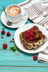 portion of Classic tiramisu dessert with raspberries and cup of espresso coffee on blue wooden background