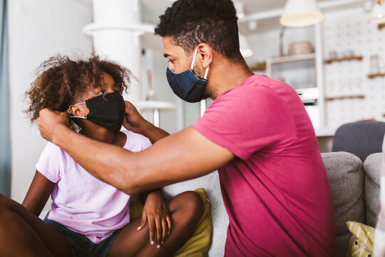 Father in a medical mask puts a protective mask on his daughter at home.Kid safety after coronavirus pandemic.