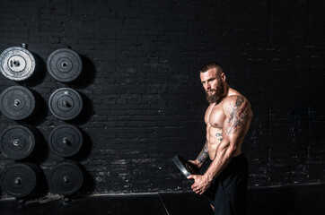 Young sweaty strong muscular fit man with big muscles holding heavy barbell weight plate in his hands preparing for hardcore cross shoulder workout training in the gym