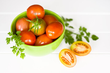 ripe tomatoes in a bowl on a white background and sprigs of parsley. tomatoes on a white background close-up. tomato halves and whole tomatoes on the table.