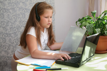 Focused kid self isolation wearing headphones using laptop in cafe, writing notes,student girl learning language, watching online webinar, Home schooling, e-learning education concept