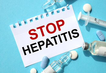 stop hepatitis. text on white paper on blue background near syringe and ampoules