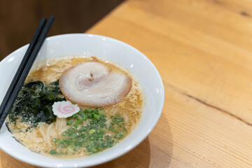 Chashu(Marinated Braised Pork) ramen served with slided seaweed and japanese bunching onion and placed on  wooden brown table.