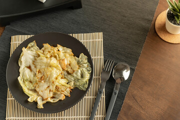 Top View and Close up on Thai Food, Stir-fried cabbage with fish sauce served in a black bowl on a bamboo placemat and decorate the table with and napkin holder and plant.