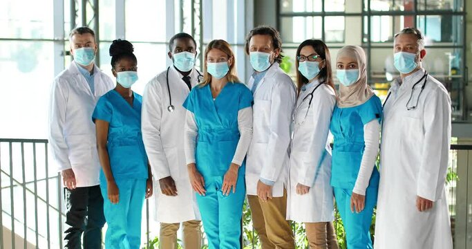 Mixed-races team of specialists, males and females doctors in hospital. International group of medics in medical masks. Protected workers. Multi ethnic physicians and nurses in uniforms in clinic.