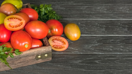 fresh ripe tomatoes and sprigs of greenery in a wooden crate on a wooden background close-up. background with red and yellow tomatoes and greens.