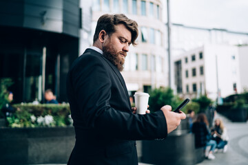 Pensive bearded businessman messaging on smartphone
