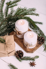 Christmas candles, gift and fir branches on a white wooden background with lights. greeting card with copy space