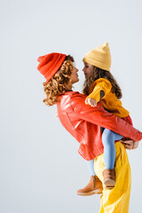 side view of mother in colorful red and yellow outfit holding daughter isolated on grey