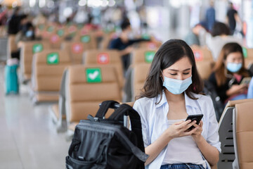 Fototapeta na wymiar Asian woman traveler who use smartphone sitting on the seat with social distancing in the airport.