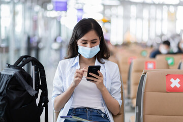Asian woman traveler who use smartphone  sitting  on the seat with social distancing in the airport.