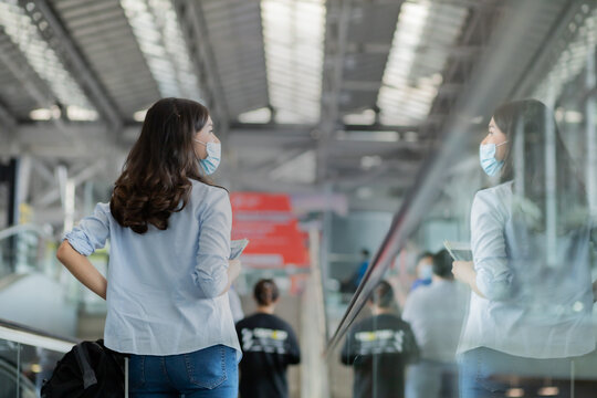 Asian traveler women wear surgical mask while standing on the sliding walkway in airport.