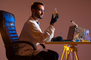 A man examines a chemical liquid in a test tube. The chemist registers the results of the experiment. A man in a white lab coat is sitting at a Desk. Microscope, laptop and test tube in the lab.