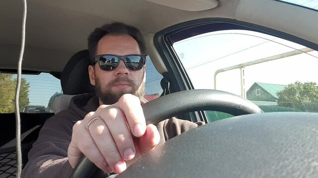 bearded man with glasses driving a car, taking a selfie with a smartphone camera