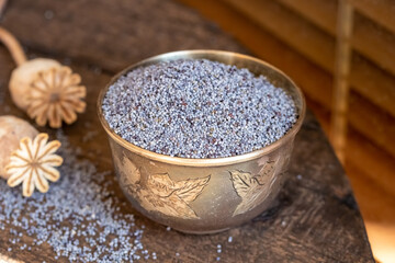 Poppy seeds in a cup with poppy pods in the background