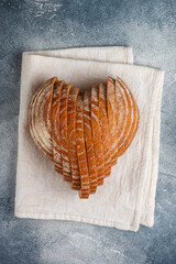 Sliced round loaf of rye bread in the shape of a heart on a gray linen napkin. Tasty and usefull home baking product close-up. Selective focus