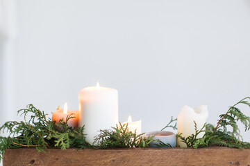 Burning candles in rustic wooden box with cedar branches on wooden table
