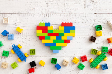 Multi-colored plastic cubes are scattered on a white wooden table. Top view of a multi-colored heart and other children's toys. Educational games for children. Early development