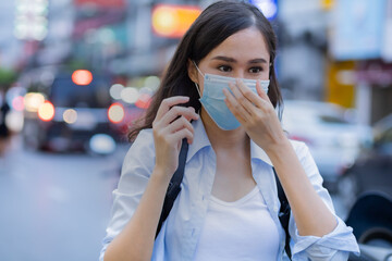 Asian traveler women wearing surgical mask while in the city with blur background.