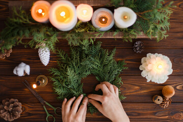 Rustic christmas wreath with candles, pine cones, scissors on wooden table, flat lay