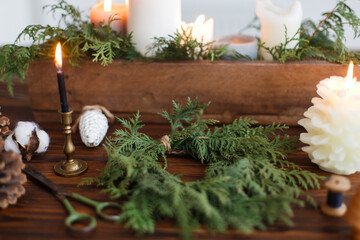 Rustic christmas wreath with candles, pine cones, thread and ornaments on wooden table.