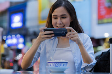 Beautiful asian woman take a  photo of her food on the table by smartphone.