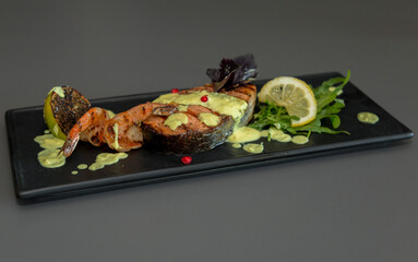 Grilled salmon with boiled shrimp in the original serving of lemon greens on a black plate.