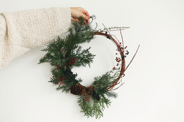 Woman in stylish knitted sweater holding modern christmas wreath on white background