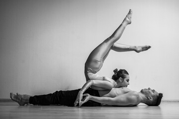A duet of acrobats showing a pair trick. A woman in gymnastics overalls in a handstand over a shirtless man lies on his back. Very flexible circus performers.