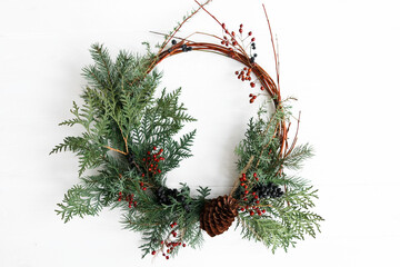 Rustic christmas wreath hanging on white wall indoors, festive holiday decoration © sonyachny